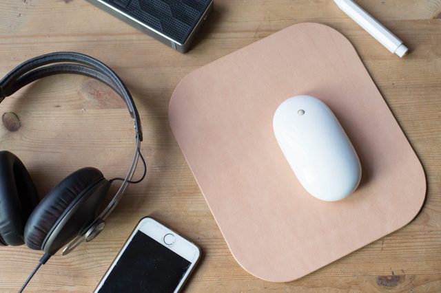 Wood work surface with a mobile phone, headphone, wireless speaker, pencil, mouse and a leather mouse pad.