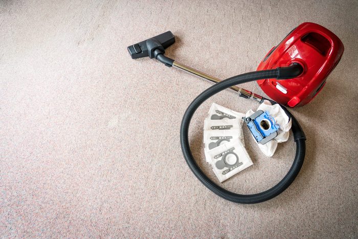 A red vacum cleaner with old and new vacum filter bags laying on a white carpet floor with spacing on the left for text. Cleaning and maintenance concept.