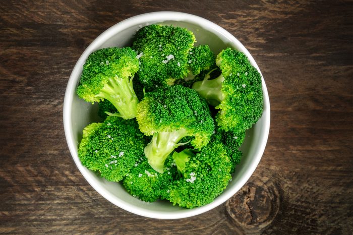 A bowl of cooked green broccoli with sea salt, shot from above on a dark wooden rustic texture with a place for text