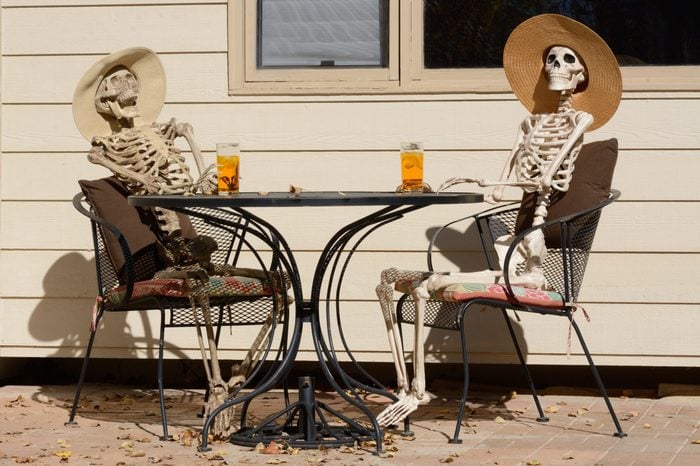 Afternoon tea shared between friends: Skeletons in hats sitting at a table outdoors