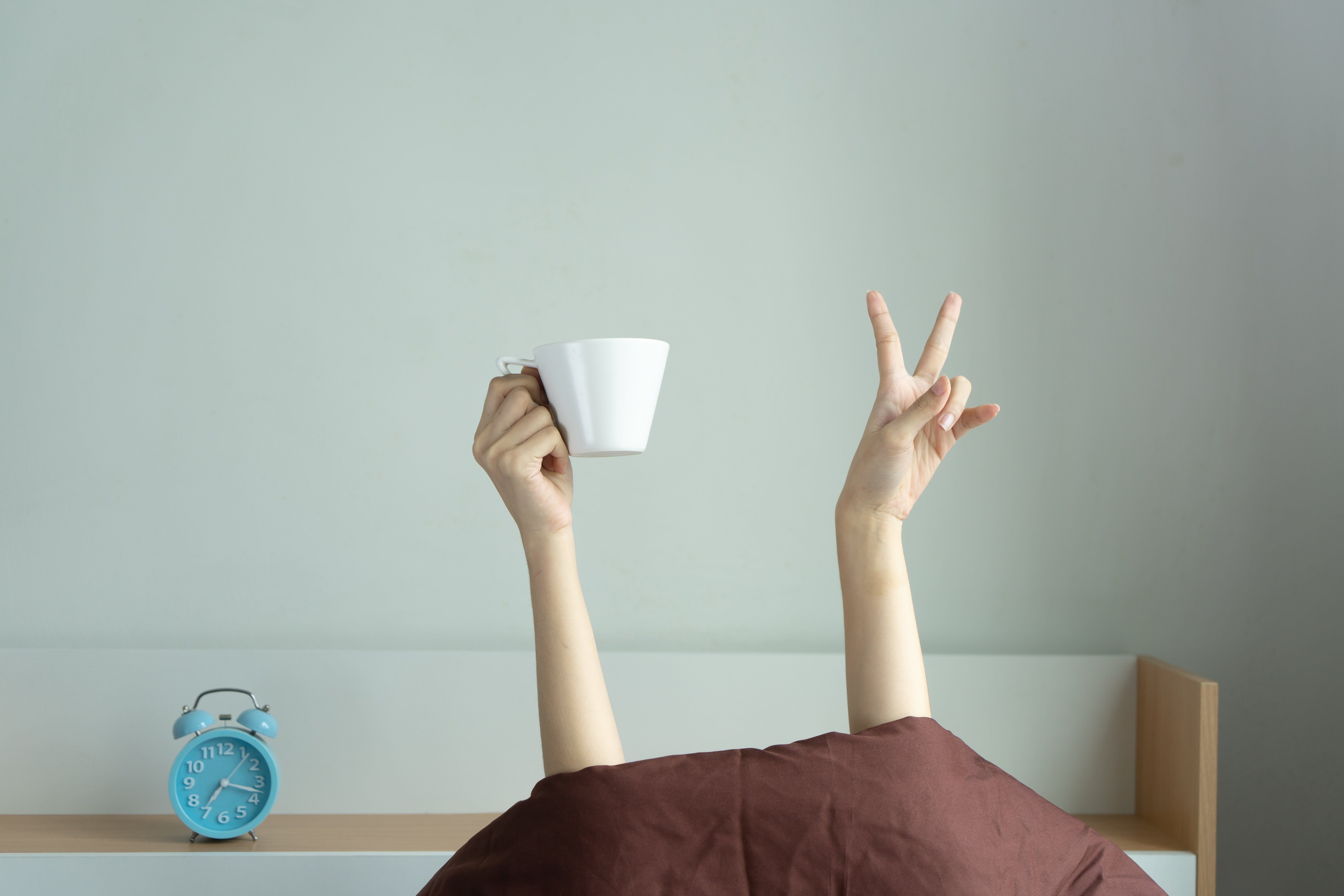 Woman showing funny v sign holding blue tea cup relaxing in bed room, Young woman with two hands drinking coffee in blue cup after awaking. wake up with fun in morning on weekend, love coffee concept.