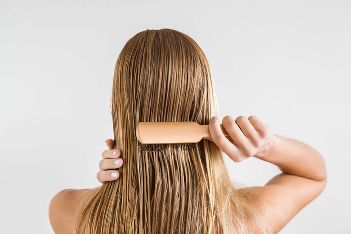 Woman with comb brushing her wet blonde hair after shower on the gray background. Cares about a healthy and clean hair. Beauty salon concept. 