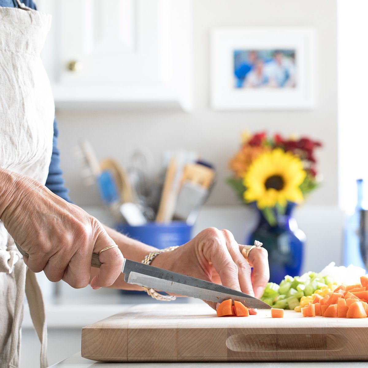 Close up photo of a woman chopping vegetables on a cutting board in a white kitchen with blue accents.