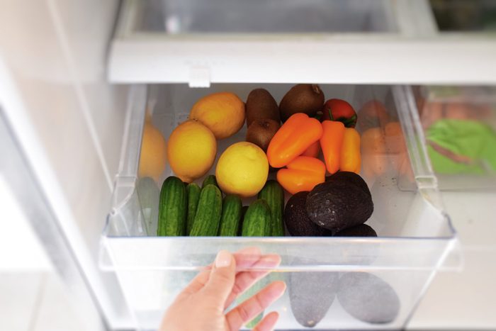 Female hand taking vegetables from a crisper drawer of a refrigerator