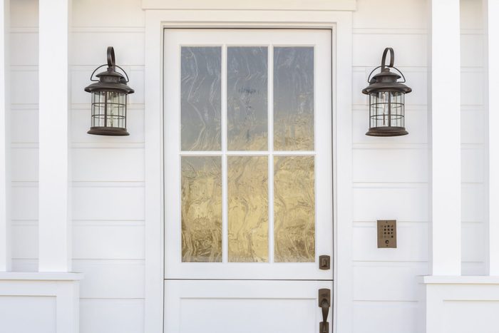 $1 solutions - Cropped horizontal shot of a white door to a classic, white, family home in daytime. The door has intricate, etched, glass detail. Also see is light fixtures, columns, and a door bell. 