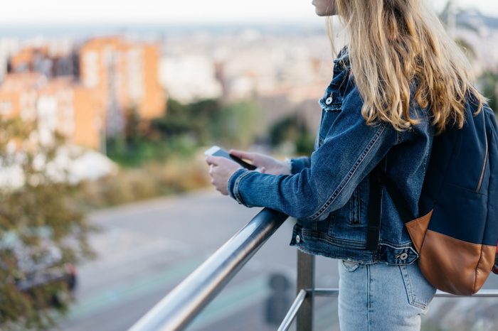 young millennial girl in a jeans jacket use smartphone, city blurring on background, space for text. woman texts to a friend. teenager with a gadget. technology and people. place for logo 
