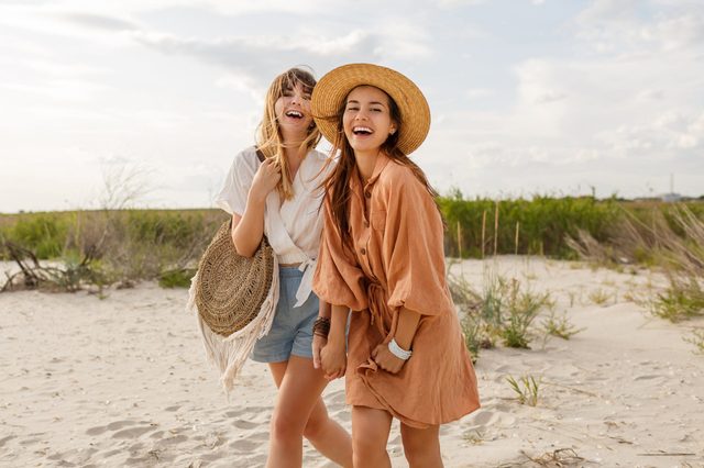 Two pretty sister girls posing on the beach, vacation mood, crazy positive feeling, summer trendy clothes and straw hat. 