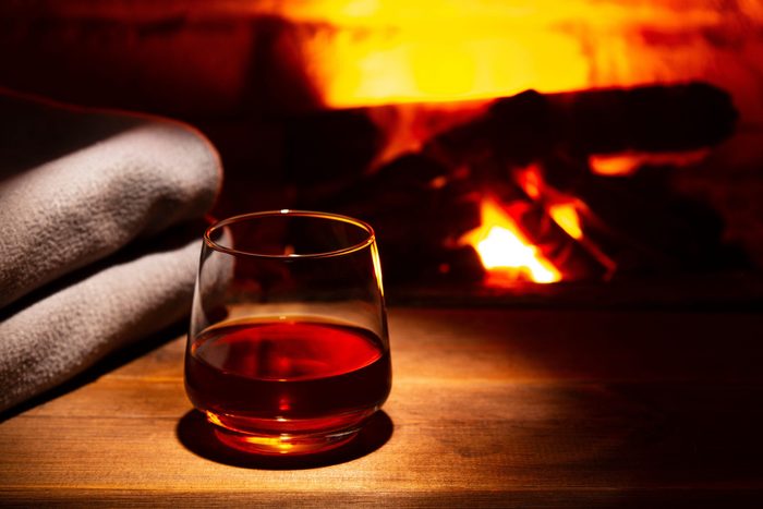 Glass of alcoholic drink wine in front of warm fireplace. Magical relaxed cozy atmosphere near fire.