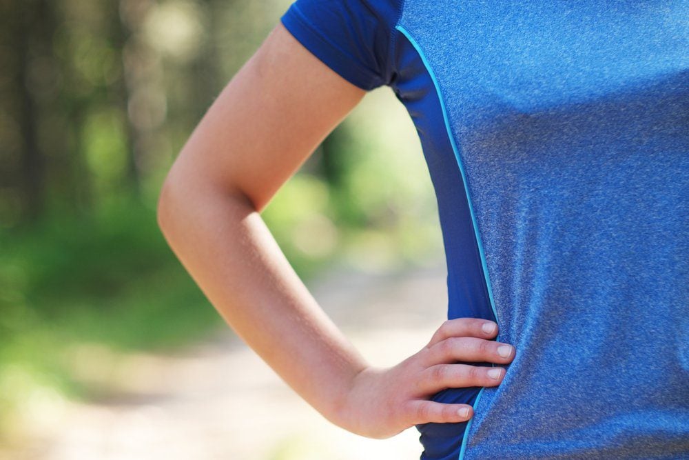 Cropped shot of fit woman in sports wear standing with her hand on hip outdoors, with sun flare.