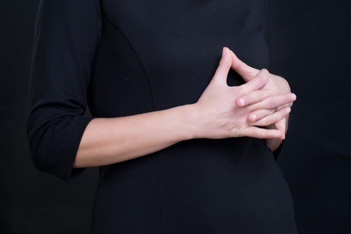 Closeup of interlaced fingers of young woman wearing black dress/ Sign of body language showing uncertainty