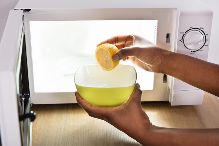 Human Hand Putting Sliced Lemon In Bowl Near Open Microwave