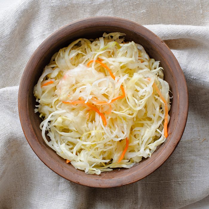 Top view of brown ceramic bowl of sauerkraut with chopped cabbage and carrot on grey towel sitting on white table surface; Shutterstock ID 1313830976; Job (TFH, TOH, RD, BNB, CWM, CM): TOH