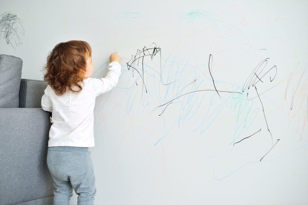 $1 solutions - Curly cute little baby girl drawing with crayon color on the wall. Works of child