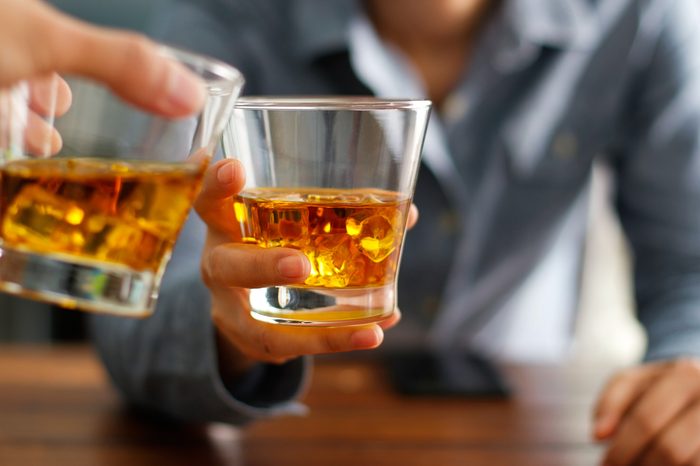Close-up of two men clink glasses of whiskey drink alcoholic beverage together while at bar counter in the pub