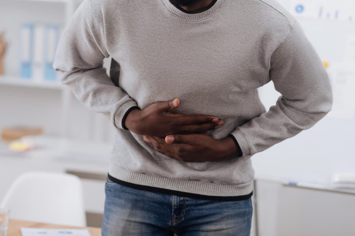 Black man in a sweater bent over and holding his stomach in pain