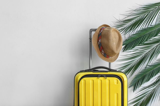 Bright yellow suitcase with hat and palm branches on light background