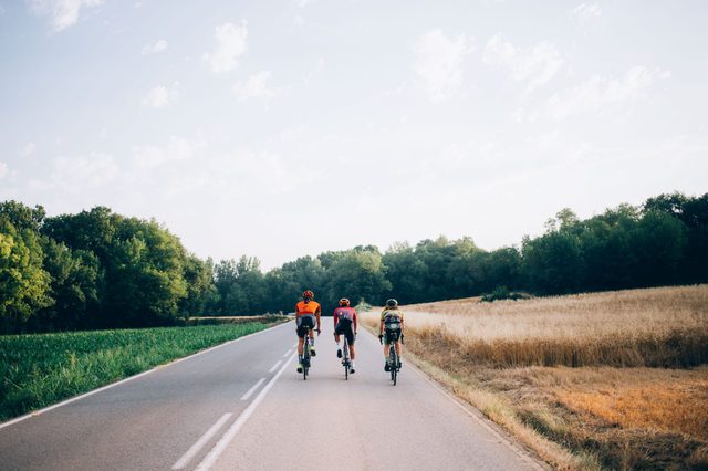 Three cyclists on road bikes ride in distance on carbon bicycles during vacation in spain, healthy lifestyle, friendship and summertime