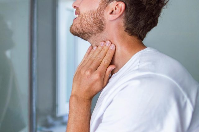 bearded man feeling his neck while looking in the mirror