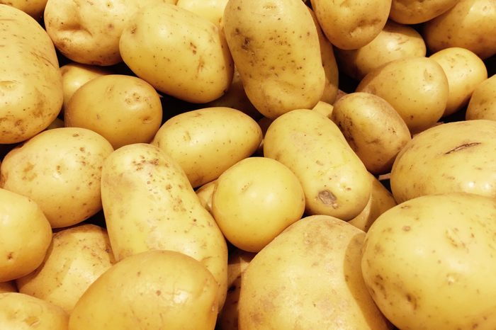 Fresh organic potato stand out among many large background potatos in the market. Heap of potatos root. Close-up potatos texture. Macro potato.