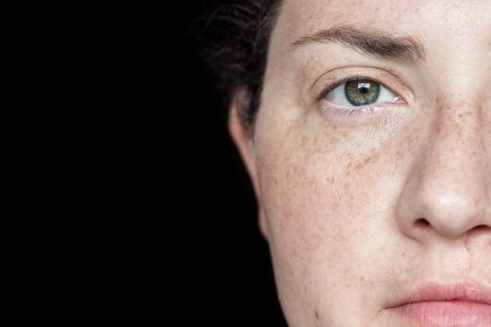 Closeup Portrait of Woman with Freckles and Green Eyes Isolated on a Black Background: Half of Face Visible on Right Side of Frame.