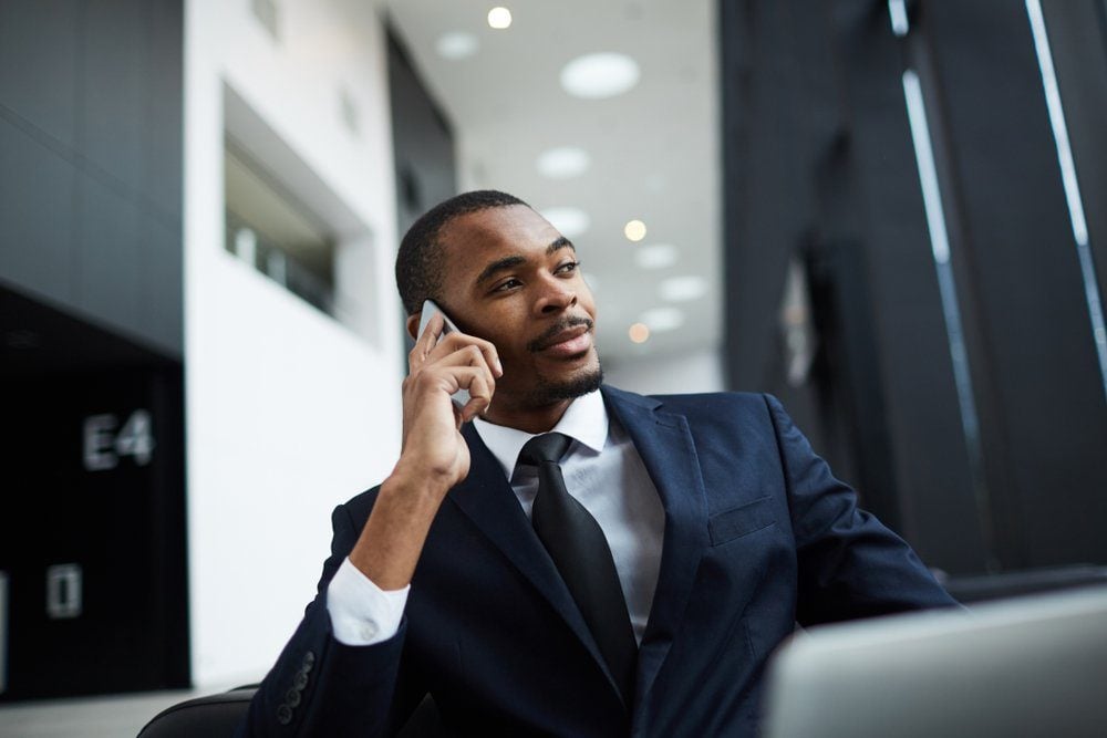 Confident young businessman of African-american ethnicity speaking by smartphone at work