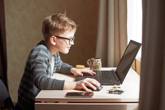 Happy boy sitting at his desk With laptop computer