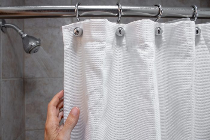 a hand pulling back a shower curtain revealing a shower head with water on horizontal shot