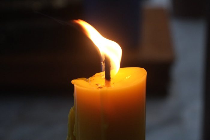 Close up burning yellow candle light against a dark blurred background