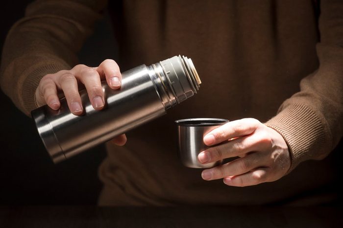 Metal thermos for trips in hand isolated on black background