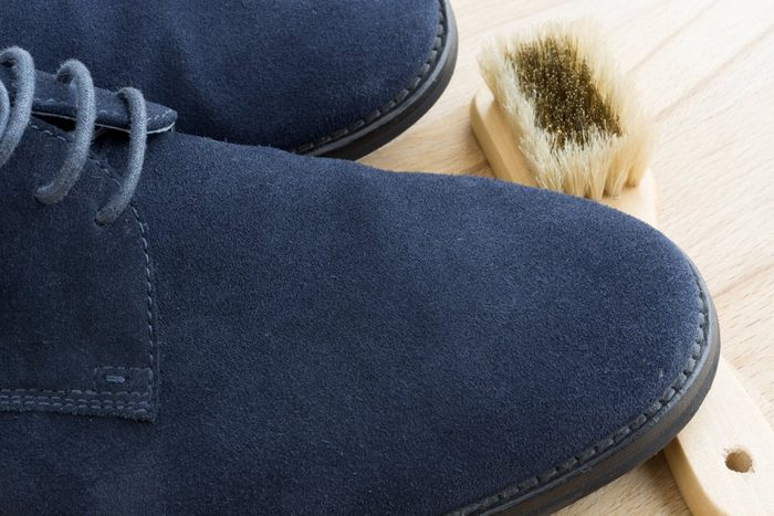 Cleaning a pair of blue suede shoes on a light wood