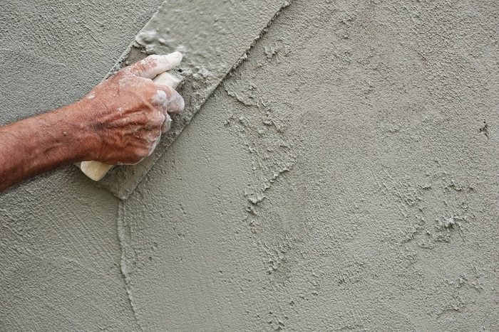Asian male house-builder hand smoothing the mortar applied on an outdoor wall with a plastering trowel.
