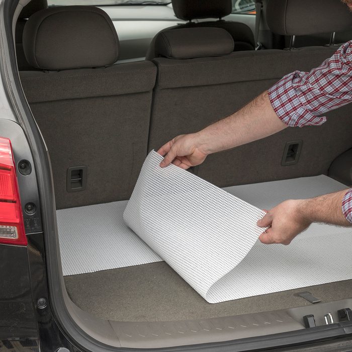 genius holiday tips - Man lining the trunk of a car with shelf liners