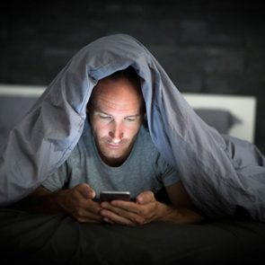 Man under covers while looking at smartphone
