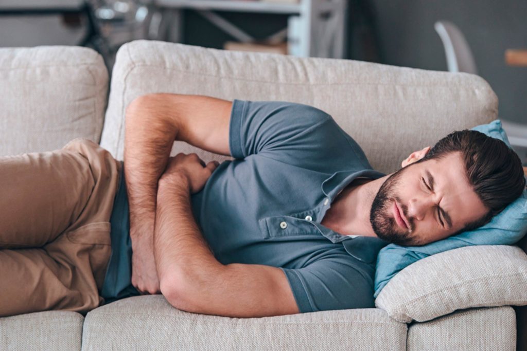 drinking too much coffee - Man clutching stomach while lying on a couch