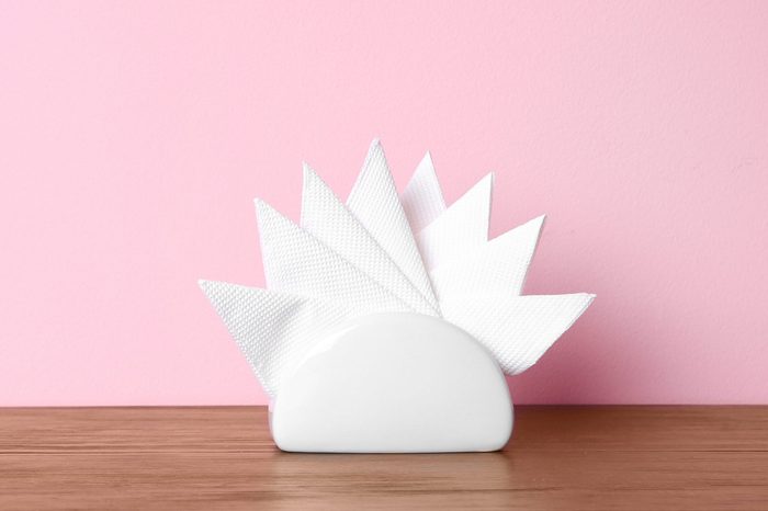 Napkin holder with paper serviettes on table against color background. Space for text