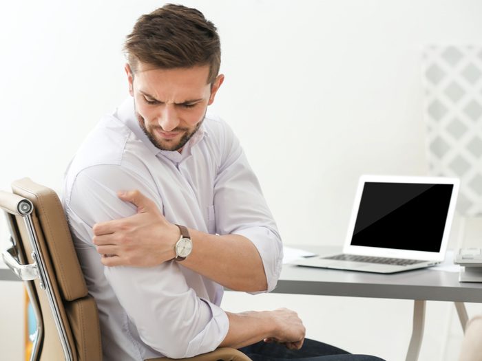 Man holding shoulder in pain at desk