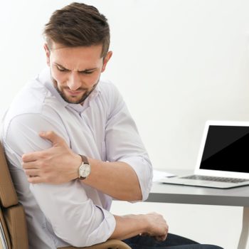 Pain management - Man holding shoulder in pain at desk