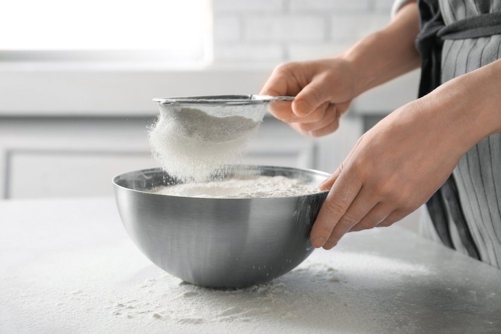 cooking mistakes - Woman sifting flour into bowl on table