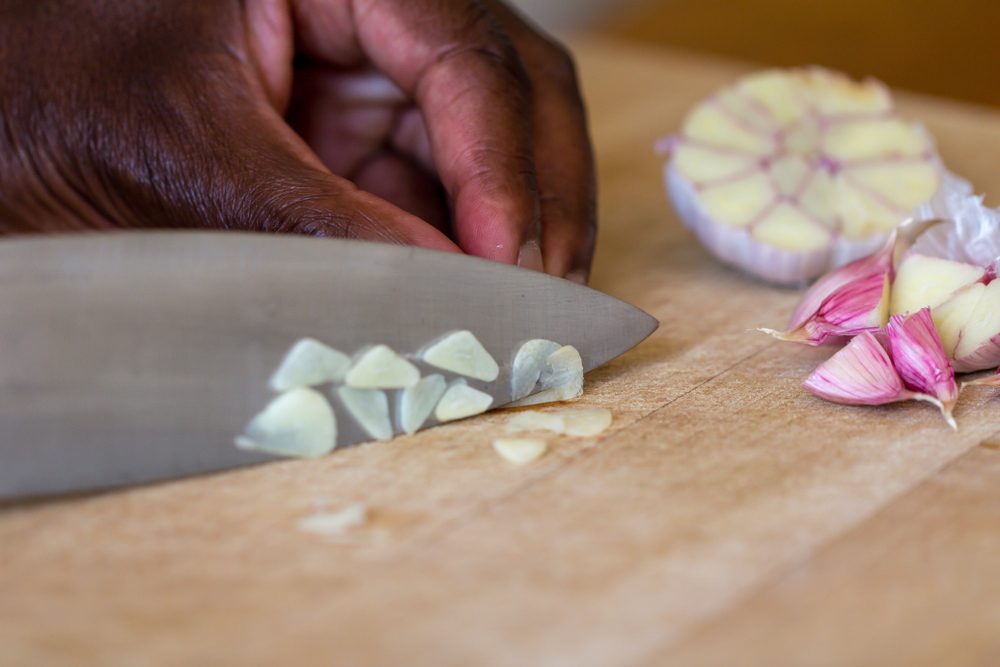 Raw garlic (Allium sativum) being chopped on a wooden chopping board