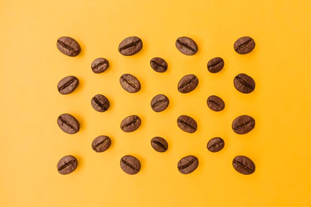 Select the best ideal coffee beans lay out on a bright orange background that emphasizes the beauty of coffee beans and perfectly blends in colors.