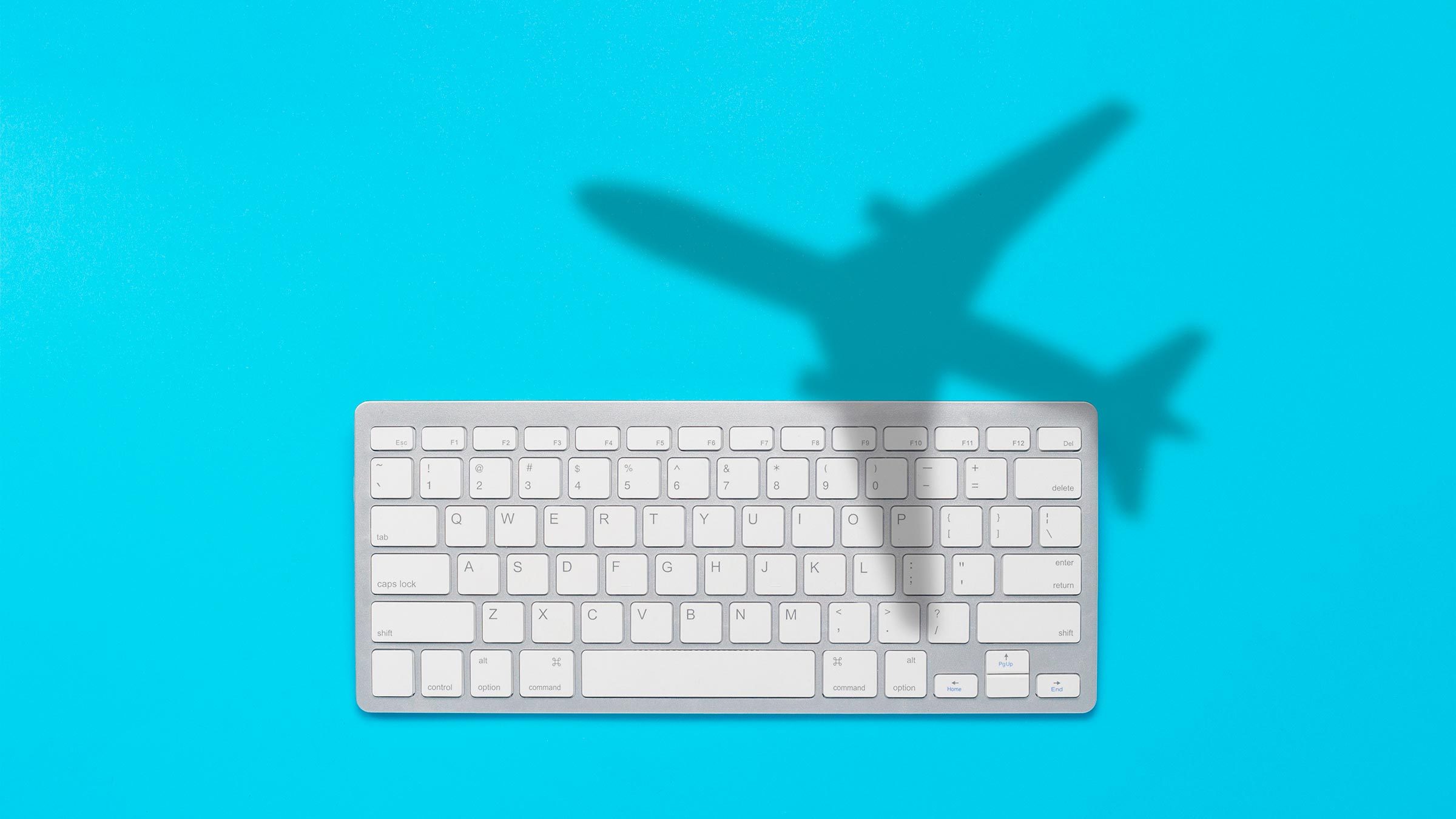 Keyboard and shadow of a flying plane on a blue background. The concept of buying tickets on the Internet online, booking tickets. Flat lay, top view.