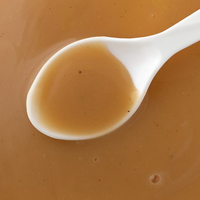 Overhead view of brown creamy turkey gravy with a white spoon in the food.; Shutterstock ID 1299945853; Job (TFH, TOH, RD, BNB, CWM, CM): TOH