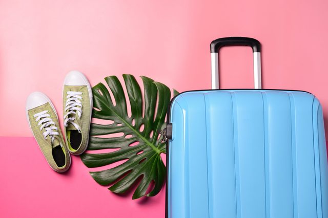 Suitcase, shoes and tropical leaf on color background. Travel concept