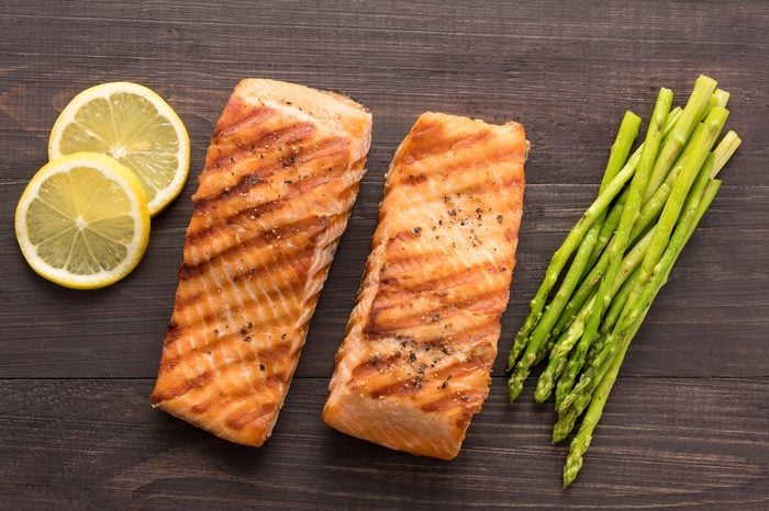 Grilled salmon with lemon, asparagus on the wooden background.