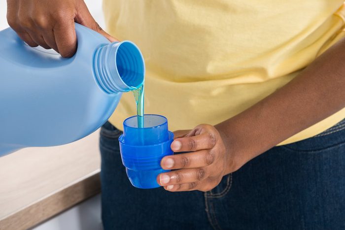 Close-up Of A Woman's Hand Pouring Detergent In The Blue Bottle Cap