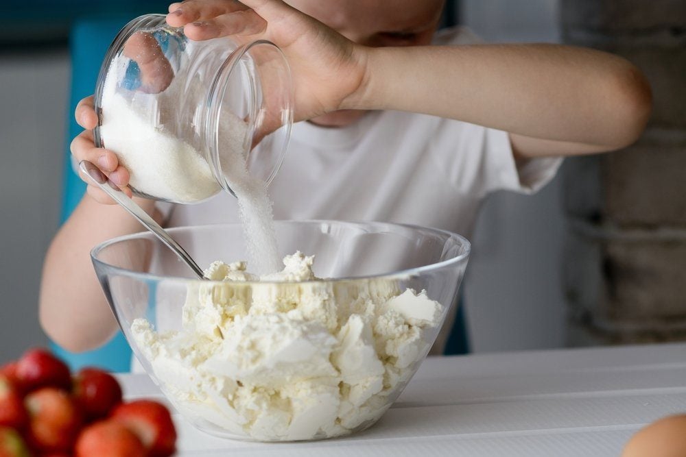 cooking mistakes - 7 year old boy adding sugar to cottage cheese in a bowl. Prepares mini cheesecakes with strawberries