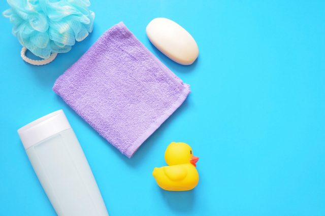 Sponge puff, shampoo bottle, purple towel, soap, yellow rubber duck on a blue background. Cosmetics for bathing babies. Flat lay bath products, top view photo. Free space for text, mock up