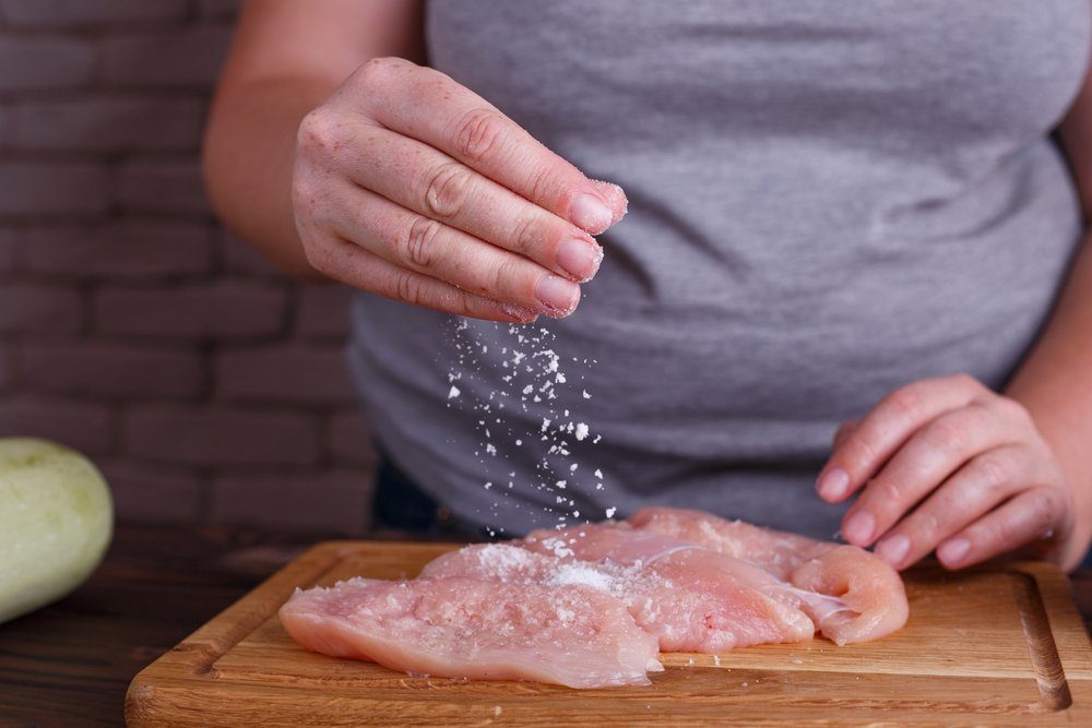 cooking mistakes - Overweight woman hands adding salt to raw chicken breasts. Dieting, healthy low calorie food, weight losing concept