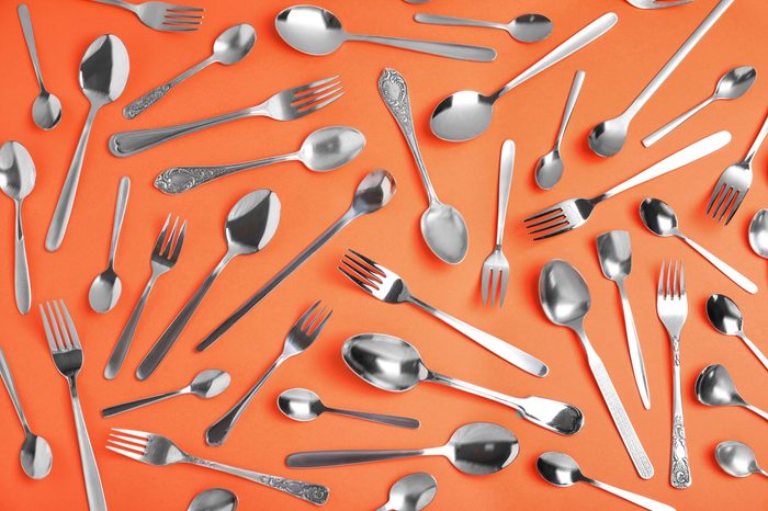 Set of new silver cutlery on coral background, flat lay