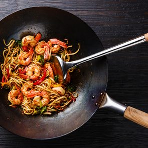 Udon stir-fry noodles with shrimp and vegetables in wok pan on black burned wooden background